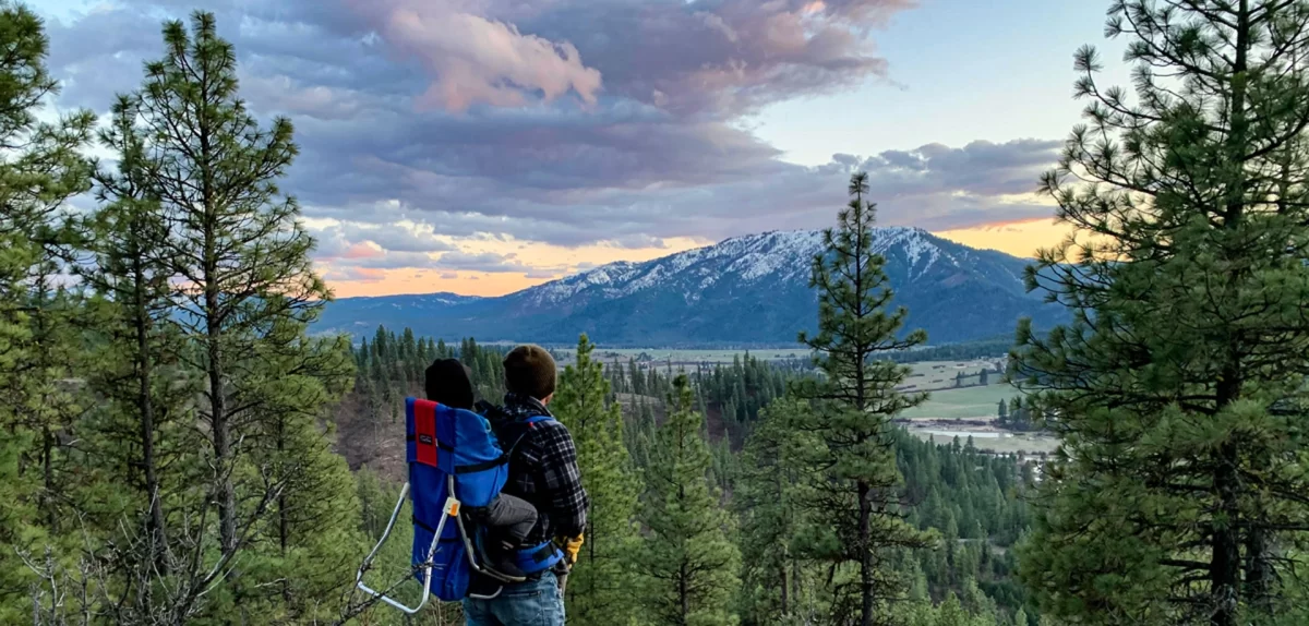 A beautiful image of a father and son looking at a colorful sunset behind a snow covered mountain after a short hike.
